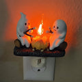Wtykowa lampka nocna LED z duchem przy ognisku na Halloween - scena z pieczeniem pianki marshmallow